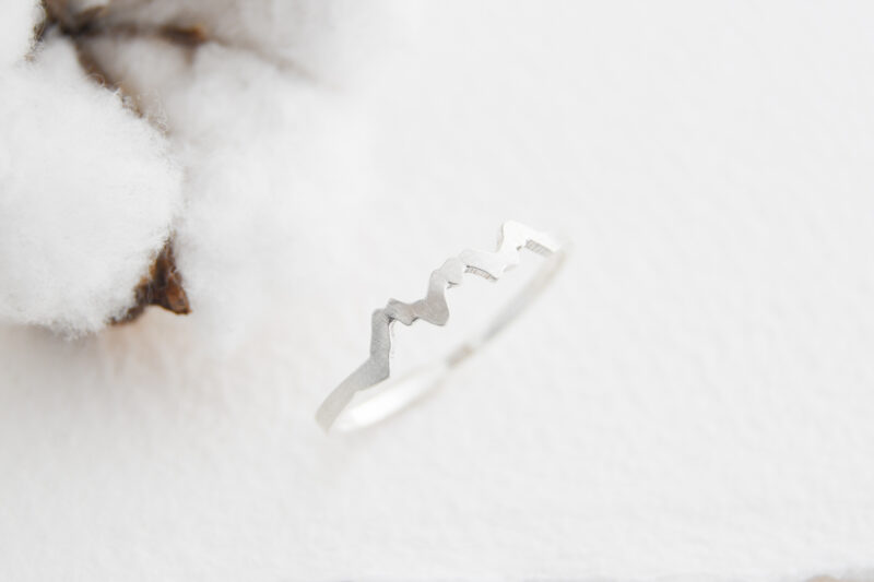 A sterling silver ring with a 3 mountain peak mountain called the 3 sisters mountain. The ring is on a white background with a cotton flower in the left hand corner.
