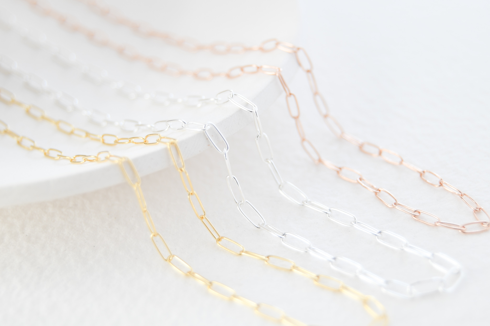 Three necklaces in paperclip style. Gold filled middle sterling silver and to the left rose gold filled. All necklaces are laying on a white dish.