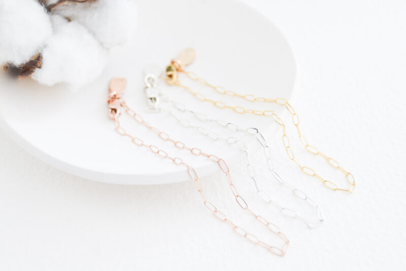 White background with a white dish. Part of a cotton flower in the left hand corner. Three bracelets lay on the white dish. Rose gold filled in the front, sterling silver in the middle and gold filled at the back
