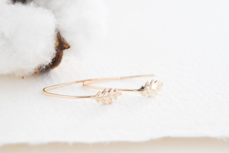White background with a cotton flower in the left corner. Arched gold filled oak leaf earrings in the middle of the photo.