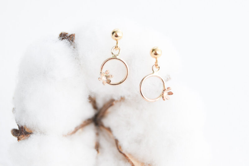 a white cotton flower in the background. Gold filled earrings on the cotton flower. Gold filled earrings with beaded studs. Gold filled circles drop down from the beaded studs. The circles have off centred flowers off to the side on the bottom of the circles.